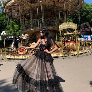 May include: A floor-length gown featuring a black lace bodice with a V-neckline and a layered skirt. The skirt consists of a beige tulle base with black tulle overlays, accented by black lace trim and scattered sequins throughout the fabric.