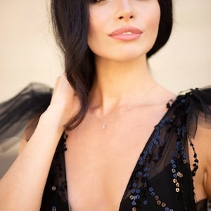 Puede incluir: Una mujer con el pelo largo y negro lleva un vestido negro de lentejuelas con un escote pronunciado. El vestido tiene una capa transparente con un delicado patr&oacute;n.
