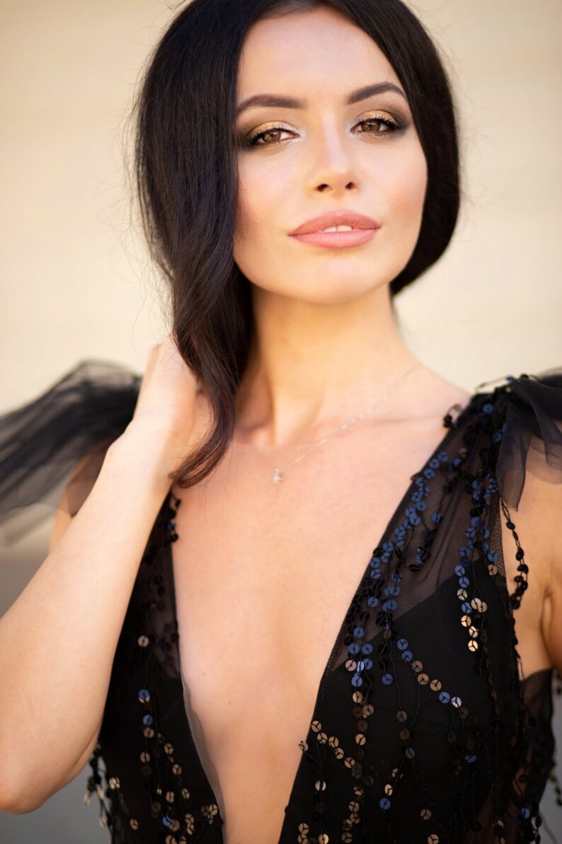 Puede incluir: Una mujer con el pelo largo y negro lleva un vestido negro de lentejuelas con un escote pronunciado. El vestido tiene una capa transparente con un delicado patr&oacute;n.