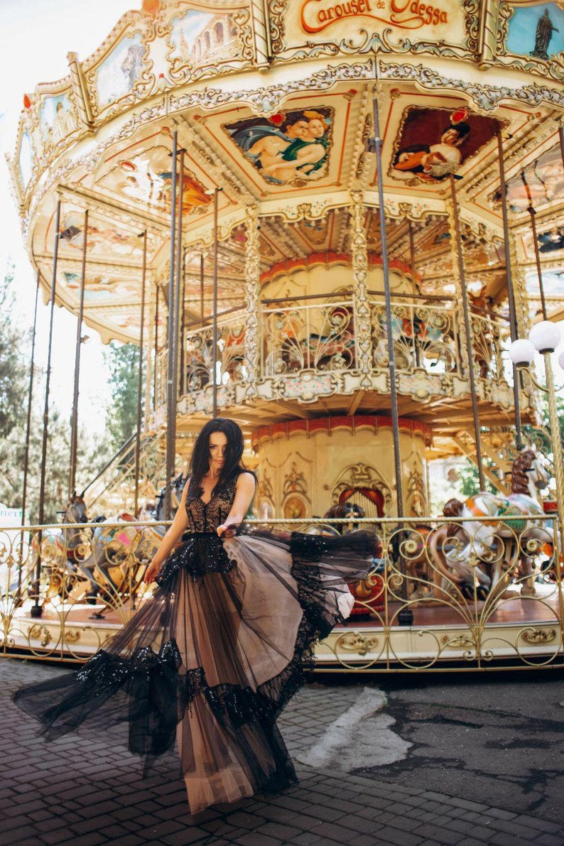 May include: A floor-length sleeveless dress featuring a black lace bodice with a deep V-neckline and a voluminous, layered tulle skirt in black and beige, accented with black sequin embellishments along the hem and waistline.