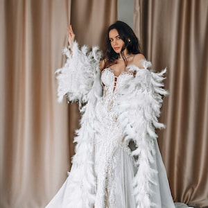 May include: A white bridal gown with a lace bodice and a long train. The gown is adorned with a white feather boa.