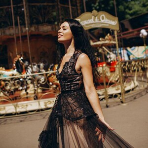 May include: A sleeveless black dress featuring a lace bodice with a V-neckline and a layered tulle skirt. The bodice is adorned with intricate black embroidery and sequins, while the skirt consists of sheer black tulle over a neutral lining.
