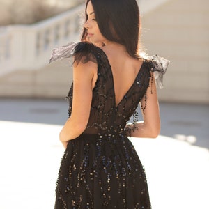 Puede incluir: Una mujer con un vestido negro de lentejuelas con mangas transparentes y un escote pronunciado. El vestido tiene una falda fluida y est&aacute; adornado con lentejuelas.