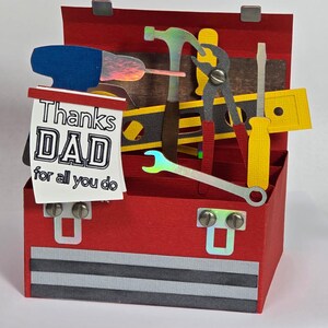 May include: A red paper toolbox with a variety of tools, including a hammer, wrench, and screwdriver. A sign inside reads "Thanks DAD for all you do". The toolbox has a gray and black striped design on the bottom.