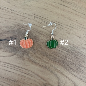May include: Two pairs of pumpkin earrings. The first pair is orange with a green stem. The second pair is green with a gold stem. #1 and #2 are written on the image.