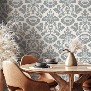 May include: A dining room set with a round wooden table and four brown chairs. The chairs have a unique cutout design. The background features a wallpaper with a gray floral pattern. A vase with dried plants sits on the table.