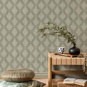 May include: A light olive green wallpaper with a repeating white fern leaf pattern. A wooden bench holds a black vase with green branches, a blue and white polka dot mug, and an open book. Two round pillows sit on the floor.