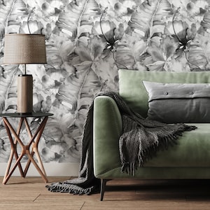 May include: A green velvet sofa with a grey throw blanket and a grey pillow with buttons. The sofa is in front of a wall with a black and white floral wallpaper.