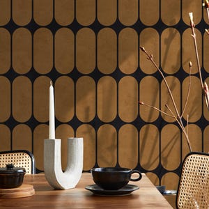 May include: A dining table set with a black and gold patterned wallpaper background. The table features a white candle in a gray holder, a black teacup and saucer, and a small black bowl. Two chairs with woven backs are visible.