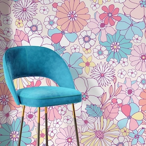 May include: A teal velvet bar stool with a curved back and gold-tipped legs stands in front of a floral wallpaper. The wallpaper features large, colorful flowers in shades of pink, blue, yellow, and white, with a light beige background.