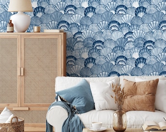 May include: A white couch with blue throw pillows and a blue throw blanket. The couch is in front of a wall with a blue and white seashell pattern wallpaper. There is a wooden cabinet with wicker doors to the left of the couch.