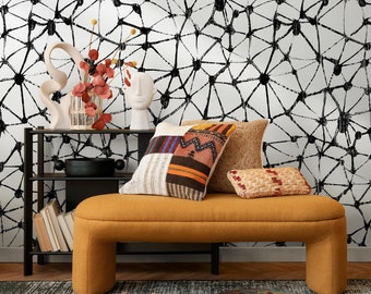 Puede incluir: Un banco amarillo mostaza con una estantería de metal negro detrás. El banco tiene dos cojines, uno con un patrón tejido y el otro con un diseño de patchwork. La pared detrás del banco está cubierta con papel tapiz abstracto en blanco y negro.
