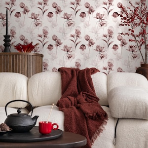 May include: A white couch with a red throw blanket on it. The couch is in front of a wall with a floral wallpaper pattern. There is a black cast iron teapot and a red mug on a wooden table in front of the couch.
