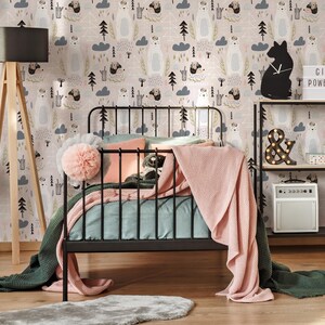 May include: A black metal bed frame with a pink and blue blanket and a fluffy white pom-pom on the bed. The wall behind the bed is covered in a pink and white wallpaper with a repeating pattern of bears, trees, and clouds.