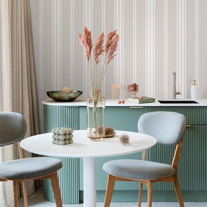 May include: A white round dining table with two gray chairs with wooden legs. The table is set with a white vase with dried pampas grass, a green decorative object, and a white napkin. The table is in front of a green cabinet with a white countertop and a white tiled backsplash.