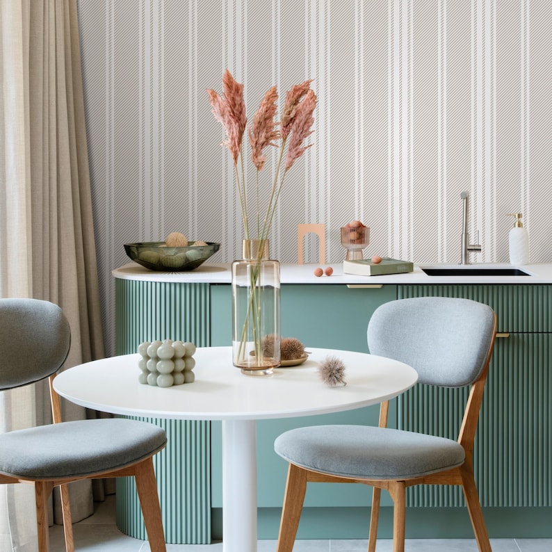 May include: A white round dining table with two gray chairs with wooden legs. The table is set with a white vase with dried pampas grass, a green decorative object, and a white napkin. The table is in front of a green cabinet with a white countertop and a white tiled backsplash.
