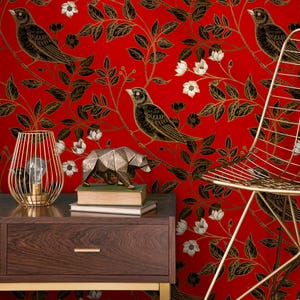 May include: A red wallpaper with a repeating pattern of black birds, leaves, and white flowers. A gold wireframe lamp, a geometric bear sculpture, and a gold chair are in the foreground, set on a dark wood nightstand.