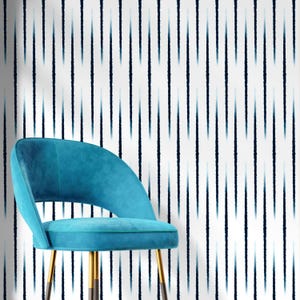 May include: A teal velvet chair with gold legs is positioned in front of a white wall with vertical blue lines. The chair has a curved back and a rounded seat. The wall pattern creates a striped effect.