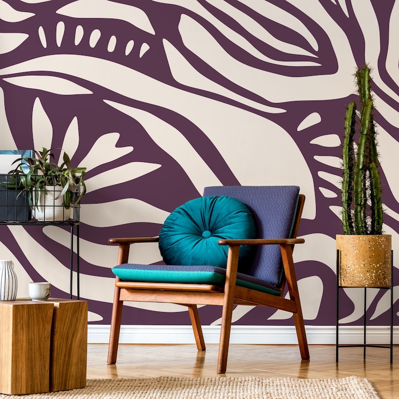 May include: A teal blue velvet cushion sits on a wooden armchair in front of a wall with a purple and white abstract pattern. A cactus plant in a brown pot sits on a black metal stand.