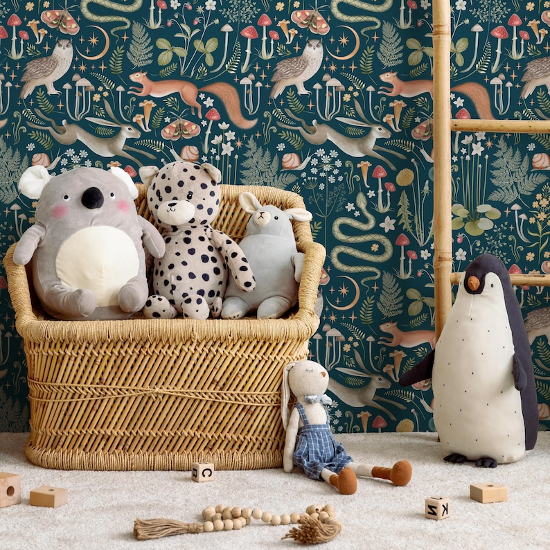 Puede incluir: Una cesta de almacenamiento de mimbre llena de animales de peluche, incluyendo un koala, un leopardo, un conejito y un ping&uuml;ino. La cesta est&aacute; delante de un papel tapiz azul verdoso con una escena de bosque caprichosa con animales, setas y plantas.