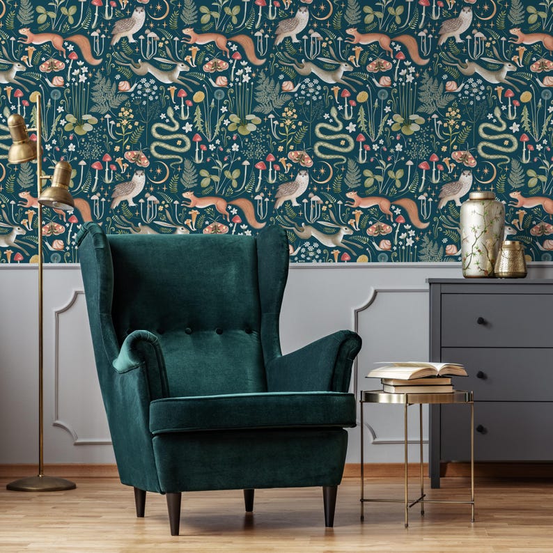 Puede incluir: Un sill&oacute;n de terciopelo verde oscuro con respaldo alto y brazos de ala se encuentra frente a una pared cubierta con un papel tapiz caprichoso que presenta un patr&oacute;n repetitivo de b&uacute;hos, ardillas, hongos y flores. El papel tapiz tiene un fondo azul oscuro con acentos coloridos.
