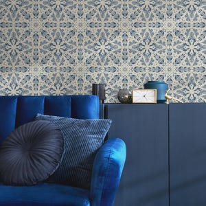 May include: A blue velvet sofa with two pillows, one black and one blue, in front of a navy blue cabinet with a clock and decorative objects. The wall behind the sofa is covered in a beige wallpaper with a blue geometric pattern.