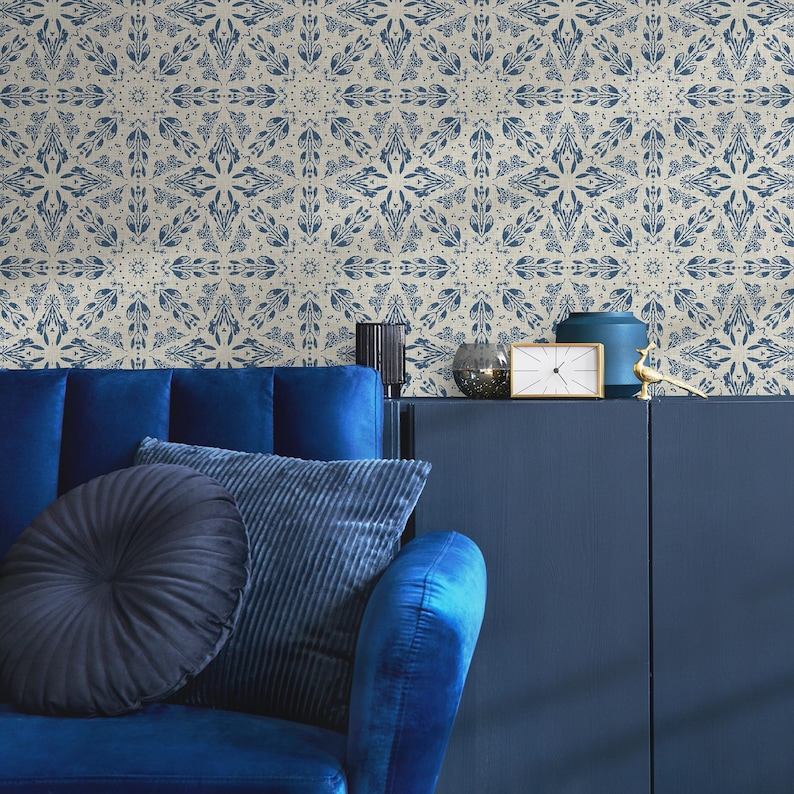 May include: A blue velvet sofa with two pillows, one black and one blue, in front of a navy blue cabinet with a clock and decorative objects. The wall behind the sofa is covered in a beige wallpaper with a blue geometric pattern.