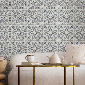 May include: A white couch with a white throw pillow and a gold metal coffee table. The coffee table has a white ceramic teapot and a white ceramic mug on it. The wall behind the couch is covered in a blue and white patterned wallpaper.
