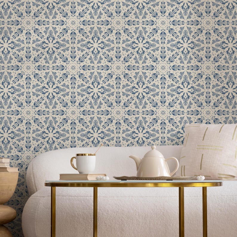 May include: A white couch with a white throw pillow and a gold metal coffee table. The coffee table has a white ceramic teapot and a white ceramic mug on it. The wall behind the couch is covered in a blue and white patterned wallpaper.