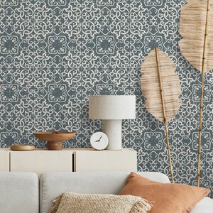 K&ouml;nnte beinhalten: Ein Wohnzimmer-Interieur mit einer grauen gemusterten Tapete, einer wei&szlig;en Lampe mit einem wei&szlig;en Lampenschirm, einer wei&szlig;en Uhr, einer Holzschale, einem wei&szlig;en Schrank und einem grauen Sofa mit braunen und beigefarbenen Kissen.