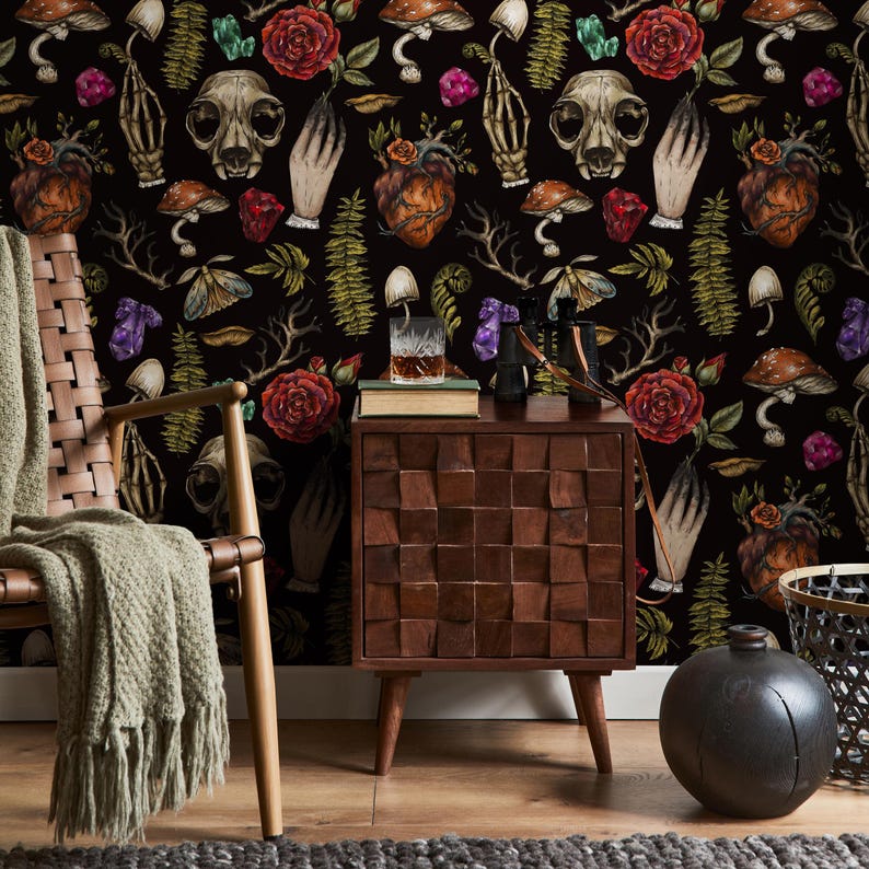 May include: A dark background wallpaper with a repeating pattern of skulls, hearts, flowers, mushrooms, and other botanical elements. The wallpaper is in a room with a wooden side table, a chair, and a decorative vase.