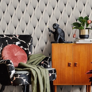 May include: A black monkey statue holding a light sits atop a wooden cabinet. A patterned armchair with a pink cushion and green throw is in front of a black and white patterned wall. A potted plant sits on top of the cabinet.