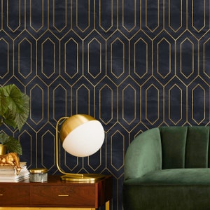 May include: A gold table lamp with a white globe shade sits on a wooden table in front of a dark blue wall with a gold geometric pattern. A dark green velvet sofa is in the background.