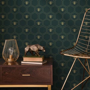 May include: A dark green wallpaper with a gold honeycomb pattern featuring bees. A gold metal chair and a gold metal lamp are in the foreground. A bronze bear figurine is on a wooden table with books.