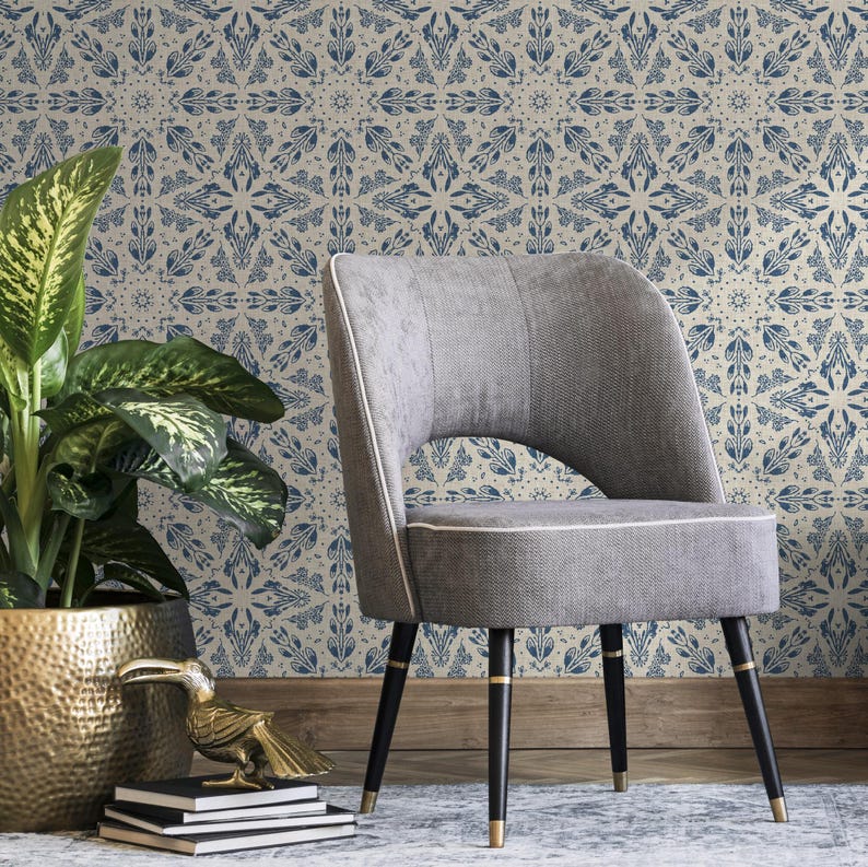 May include: A gray upholstered chair with black legs and gold accents sits in front of a wall covered in blue and white patterned wallpaper.