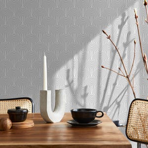 May include: A wooden table is set with a black teacup and saucer, a small black pot, and a decorative candle holder with a white candle. The background features a gray and white geometric wallpaper.