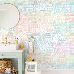 Peut inclure: Une salle de bain avec un papier peint coloré présentant un motif répété de maisons en lignes aux couleurs pastel. La pièce comprend un lavabo blanc, un miroir rond et un meuble vert menthe. Un porte-serviettes doré maintient une serviette à motifs.
