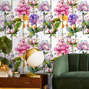 May include: Watercolor floral wallpaper featuring pink and purple peonies with green leaves and buds. The design includes colorful paint splatters on a white background. A gold and white lamp sits on a wooden table.