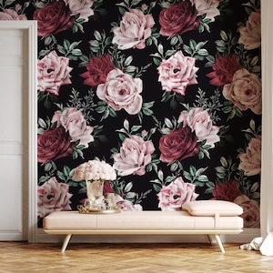 May include: A floral wallpaper featuring a repeating pattern of large roses in shades of pink and burgundy against a black background. Green leaves and stems are interspersed among the flowers. A light pink bench with a gold tray and vase of flowers is in front of the wallpaper.