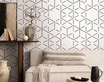 May include: A living room scene featuring a white sofa with a striped pillow and a wooden side table. The wall is decorated with a geometric black and white pattern. A vase with branches and a decorative pitcher are also visible.