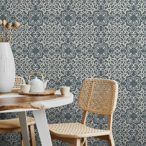 K&ouml;nnte beinhalten: Zwei St&uuml;hle mit geflochtenen Sitzen und R&uuml;ckenlehnen stehen an einem Holztisch vor einer Wand, die mit einer blauen und wei&szlig;en gemusterten Tapete bedeckt ist. Die Tapete hat einen abgenutzten Look und zeigt ein sich wiederholendes geometrisches Muster.