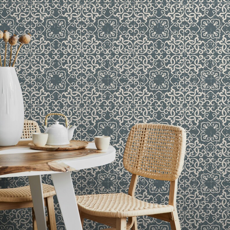 K&ouml;nnte beinhalten: Zwei St&uuml;hle mit geflochtenen Sitzen und R&uuml;ckenlehnen stehen an einem Holztisch vor einer Wand, die mit einer blauen und wei&szlig;en gemusterten Tapete bedeckt ist. Die Tapete hat einen abgenutzten Look und zeigt ein sich wiederholendes geometrisches Muster.