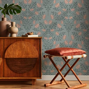 May include: A wooden stool with a red cushion sits in front of a wall covered in a floral wallpaper with a repeating pattern of pink flowers and green leaves on a light blue background.