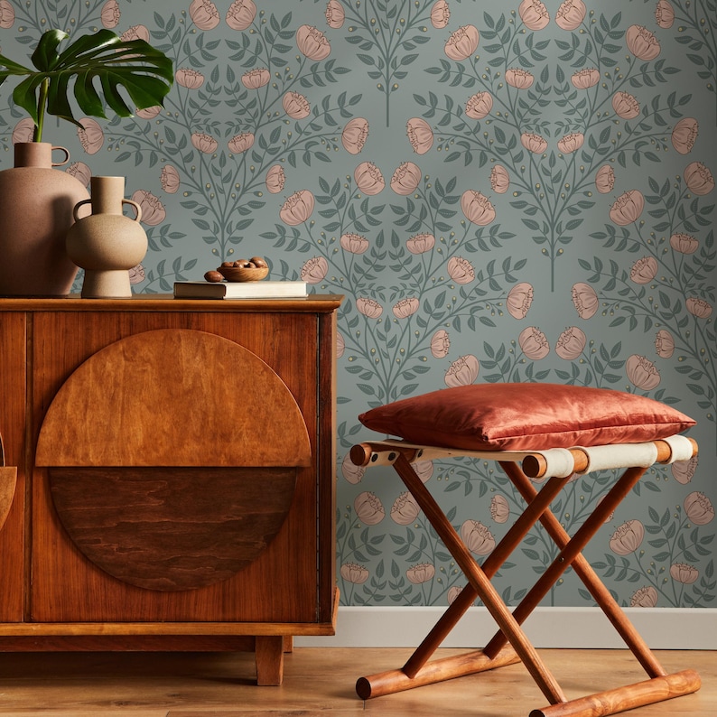 May include: A wooden stool with a red cushion sits in front of a wall covered in a floral wallpaper with a repeating pattern of pink flowers and green leaves on a light blue background.