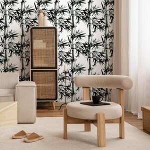 May include: A modern living room with a bamboo-patterned wallpaper. The room features a light wood chair with a round seat, a woven cabinet, and a beige sofa. A black mug and a small notebook sit on the chair.