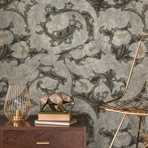 May include: A dark brown wooden nightstand holds a gold wire lamp, a stack of two books, and a bronze-colored geometric bear figurine. The background features wallpaper with a repeating pattern of large, light gray acanthus leaves and flowers.
