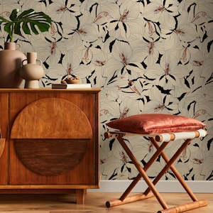 May include: A wooden cabinet with a half-circle design, two vases, and a leafy plant sits in front of a floral wallpaper. A small wooden stool with a red cushion is in the foreground. The wallpaper features a cream background with black and light brown floral patterns.