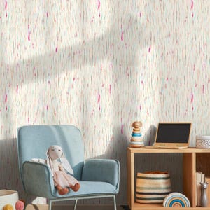 May include: A light blue armchair with a stuffed bunny sits in front of a wall covered in off-white wallpaper with vertical streaks of pink, orange, and blue. A small wooden table holds a laptop, toys, and a woven basket.