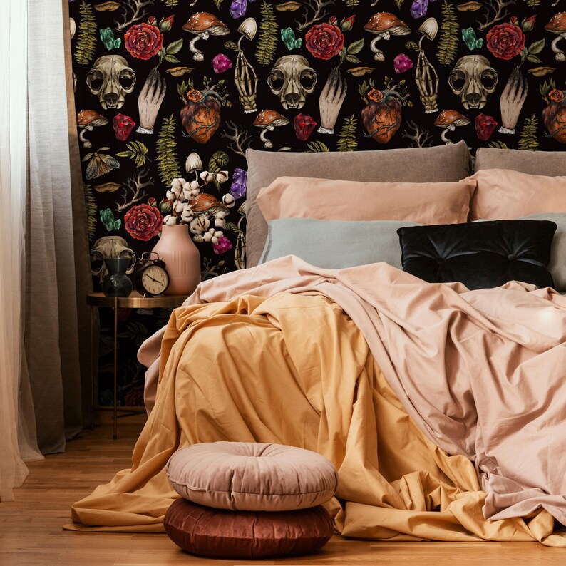May include: A black and white patterned wallpaper with a skull, flowers, and other botanical elements. A bed with a light brown comforter and a pink and brown throw pillow is in front of the wallpaper.