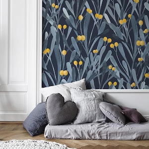 Könnte beinhalten: Dunkelblaue Tapete mit einem Aquarelldesign aus grauen Blättern und gelben Beeren. Mehrere Kissen in Grau- und Lilatönen sind auf einer grauen Matratze auf einem Holzboden angeordnet. Ein herzförmiges Kissen befindet sich in der Mitte.